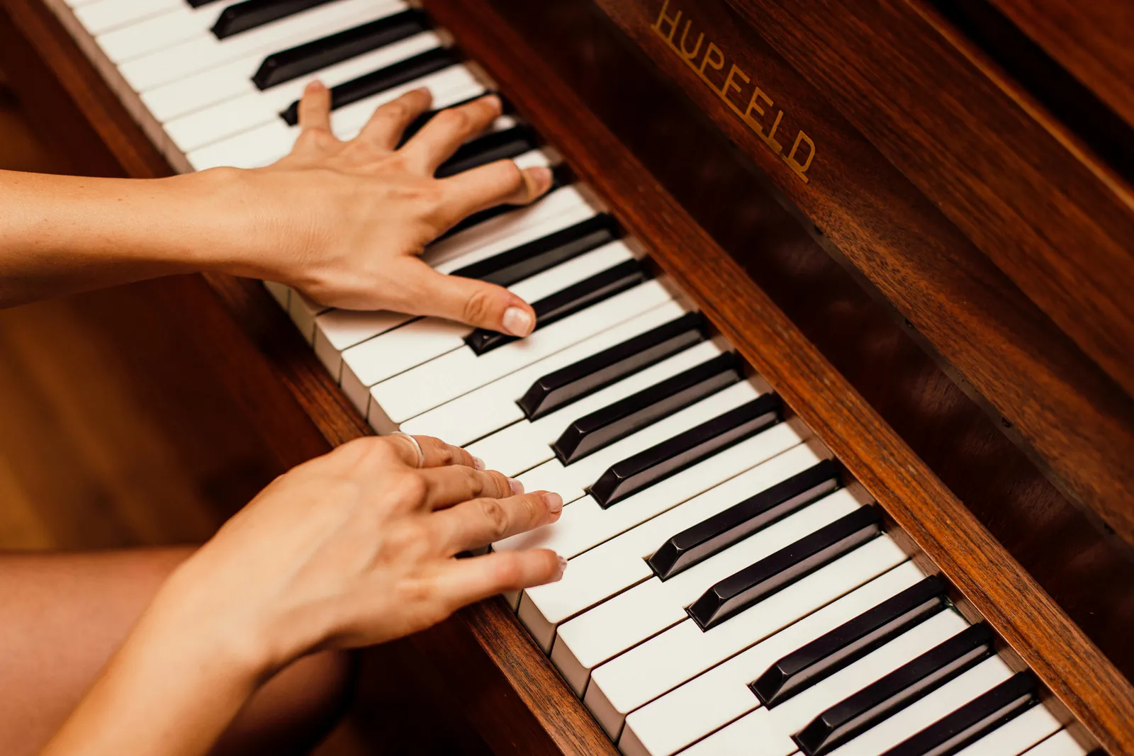Hands playing an upright piano